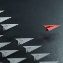 Leadership concept with red paper plane leading among white ones on black background